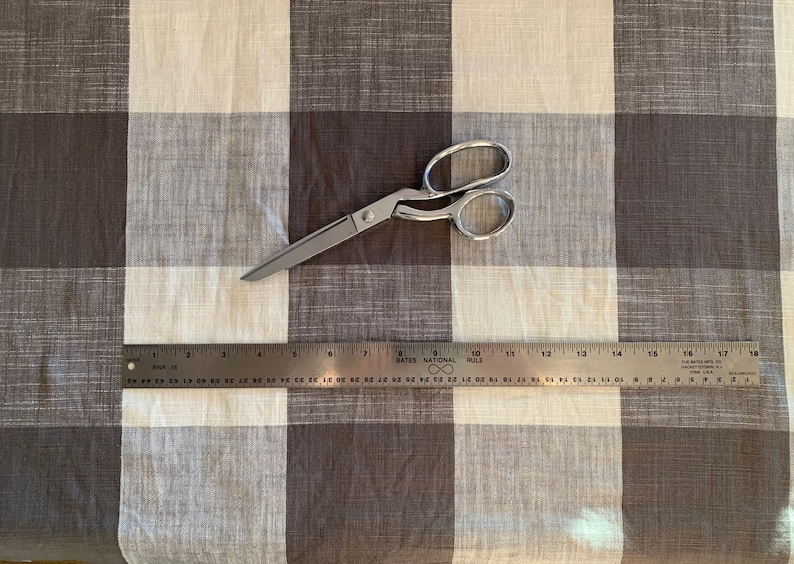 May include: A brown and white checkered fabric with a pair of silver scissors and a ruler. The ruler is marked with inches and has the text "Bates National Rule" printed on it.
