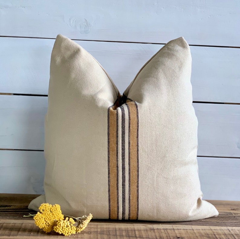 May include: A cream-colored pillow with brown and tan stripes down the center. The pillow is sitting on a wooden surface.