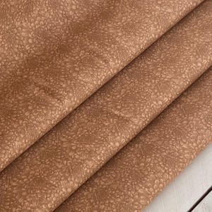 Puede incluir: Primer plano de una tela marrón con un sutil estampado floral en relieve. La tela tiene un tacto suave y texturizado.