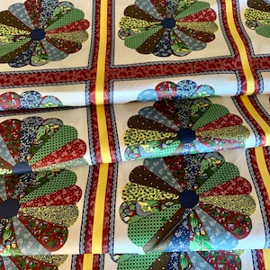 May include: White fabric with a repeating pattern of blue, green, red, and yellow patchwork circles. The circles are made up of smaller pieces of fabric sewn together in a radial pattern.