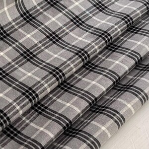 May include: Gray and black plaid fabric with a soft, woven texture. The fabric is folded in thirds, showing the pattern from different angles.