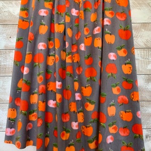 May include: Gray fleece fabric with a repeating pattern of orange and pink apples. The apples have green leaves and are arranged in a random pattern.