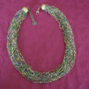 May include: A gold chain necklace with multiple strands of tiny colorful beads. The necklace is on a red background.