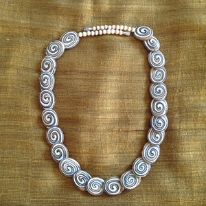 May include: A white and brown necklace made of oval-shaped beads with a spiral pattern. The necklace is on a brown fabric background.