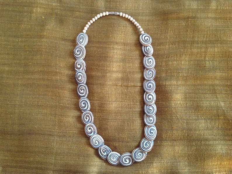 May include: A white and brown spiral patterned necklace with a silver clasp.