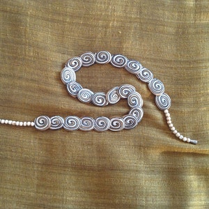 May include: A white and black spiral patterned necklace with a long strand of white beads.