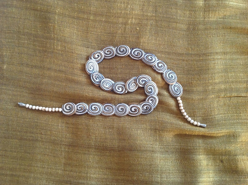 May include: A white and black spiral patterned necklace with a long strand of white beads.