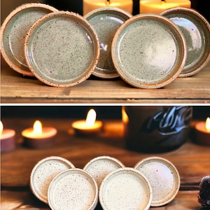 May include: A collection of handmade ceramic coasters. The coasters have a speckled, light green glaze with a natural, unglazed rim. The image shows the coasters arranged on a wooden surface, with lit candles in the background, creating a warm, inviting atmosphere.