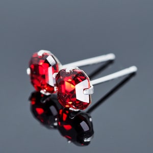 May include: A pair of silver stud earrings with red gemstone accents. The earrings are on a black surface.
