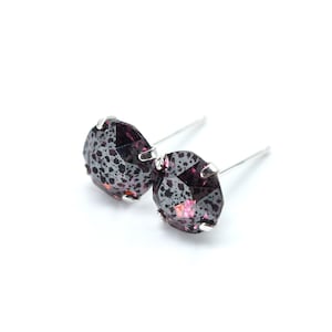 May include: A pair of silver stud earrings with a dark purple, faceted gemstone. The gemstone has a speckled pattern with a hint of pink.
