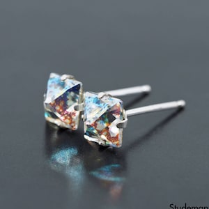 May include: A pair of silver stud earrings with iridescent square-shaped crystals. The crystals have a blue, green, and orange color scheme.
