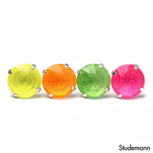 May include: Four colorful stud earrings in yellow, orange, green, and pink. Each earring features a large, round, faceted gemstone set in a silver-colored metal. The earrings are arranged horizontally against a white background.