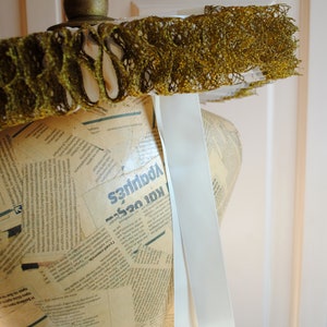 K&ouml;nnte beinhalten: Eine wei&szlig;e Schneiderpuppe, die mit Zeitungsartikeln und einem wei&szlig;en Band bedeckt ist. Die Schneiderpuppe tr&auml;gt einen goldenen und wei&szlig;en Spitzenkragen.