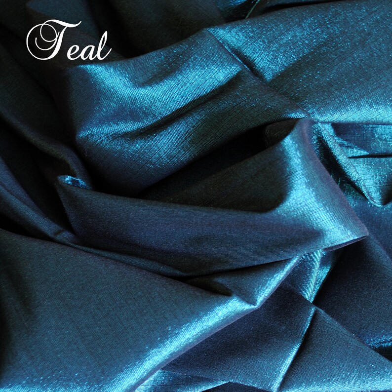 May include: Teal fabric with a shimmery, iridescent finish. The fabric is folded and draped, showing its texture and sheen.