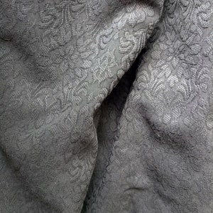 May include: Close-up of a black fabric with a subtle embossed floral pattern. The fabric is wrinkled and folded, showing the texture of the material.