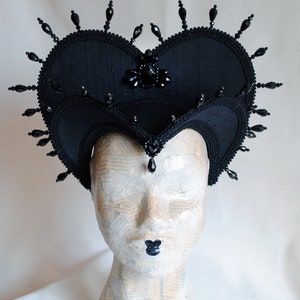 May include: A black heart-shaped headpiece with black bead embellishments and a black jewel in the center.