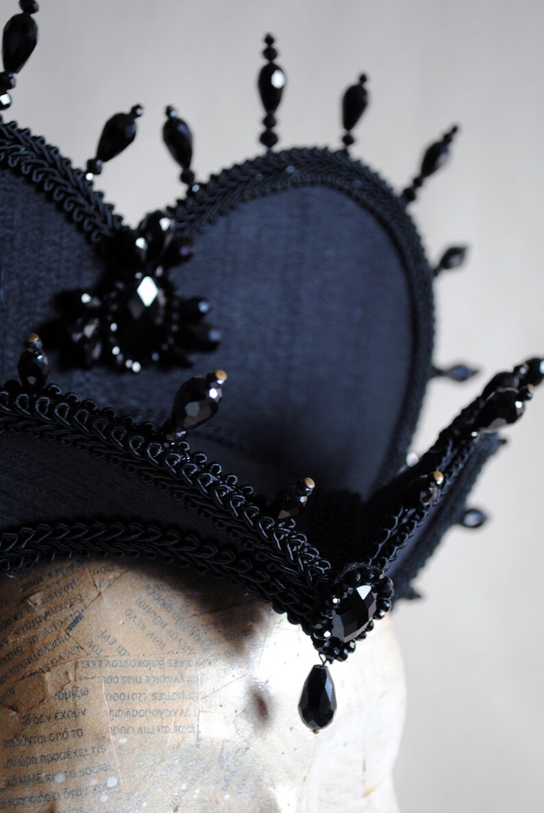 May include: A black crown with a heart-shaped base and black bead embellishments. The crown is made of fabric and has a black lace trim.