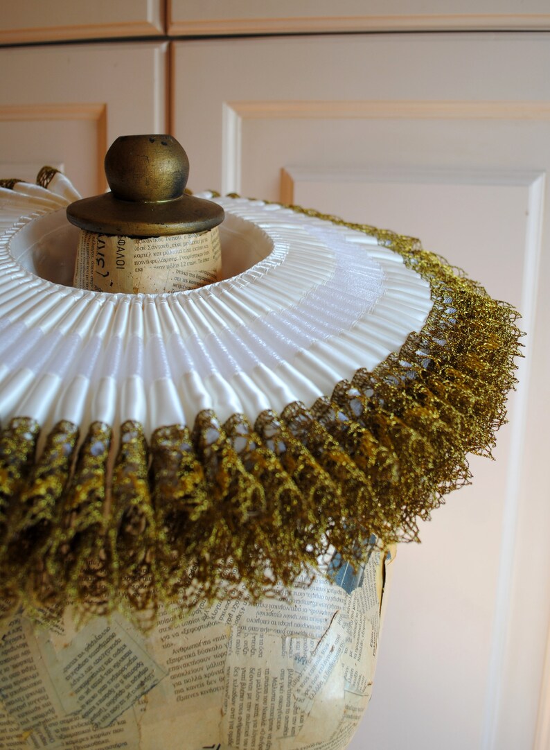 K&ouml;nnte beinhalten: Ein wei&szlig;er R&uuml;schenkragen mit goldener Spitzenborte. Der Kragen befindet sich auf einem Mannequin-Kopf und ist aus einem weichen, zarten Stoff gefertigt.