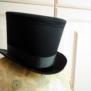 May include: A black top hat with a black satin band. The hat is sitting on a mannequin covered in printed paper.