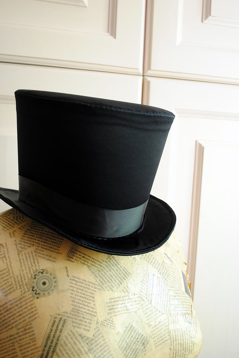 May include: A black top hat with a black satin band. The hat is sitting on a mannequin covered in printed paper.
