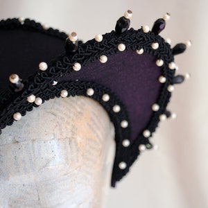 May include: A black headband with a purple fabric base and a black lace trim. The headband is decorated with white pearls and black beads.