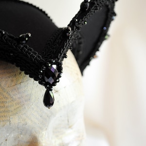 May include: A black lace headband with a large black gemstone pendant. The headband is decorated with black beads and has a pointed shape.
