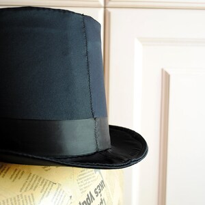May include: A black top hat with a black satin band. The hat is sitting on a mannequin head covered in newspaper.