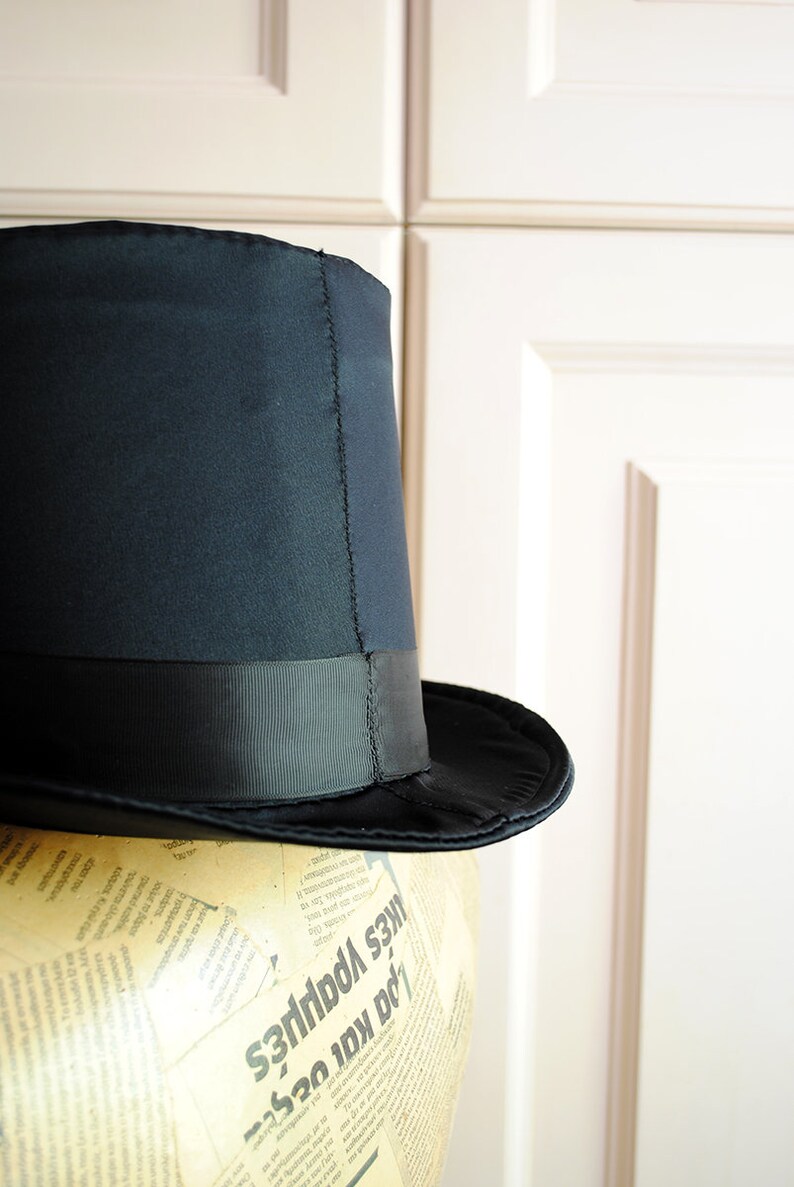 May include: A black top hat with a black satin band. The hat is sitting on a mannequin head covered in newspaper.