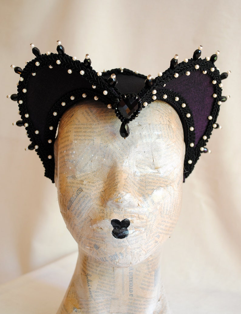 May include: A black felt headpiece with a pointed crown and curved sides. The headpiece is decorated with black and white beads and a large black gemstone.