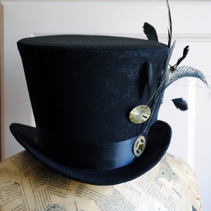 May include: Black top hat with a decorative clock and feather accents. The hat features a black ribbon band and a gear embellishment. The hat is displayed on a mannequin head, showcasing its shape and design.
