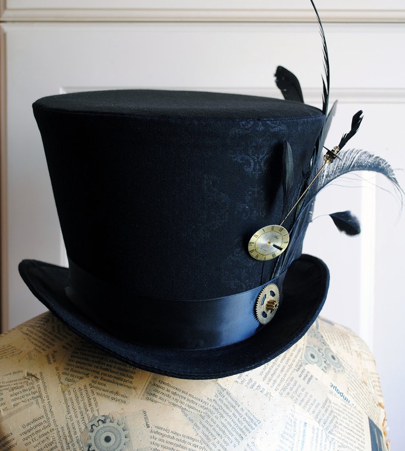 May include: Black top hat with a decorative clock and feather accents. The hat features a black ribbon band and a gear embellishment. The hat is displayed on a mannequin head, showcasing its shape and design.
