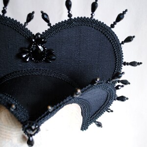 May include: A black fabric crown with a large black jewel in the center and black beads around the edges.