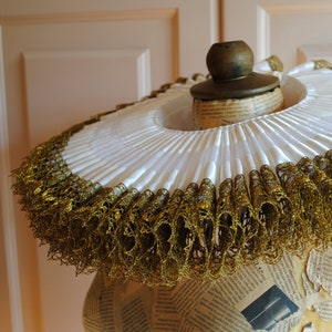 K&ouml;nnte beinhalten: Ein wei&szlig;er R&uuml;schenkragen mit goldener Spitzenborte. Der Kragen befindet sich auf einer mit Zeitungspapier bedeckten Schaufensterpuppe.