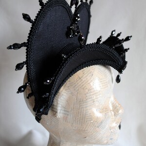 May include: A black fabric headpiece with a heart shape and black bead embellishments.