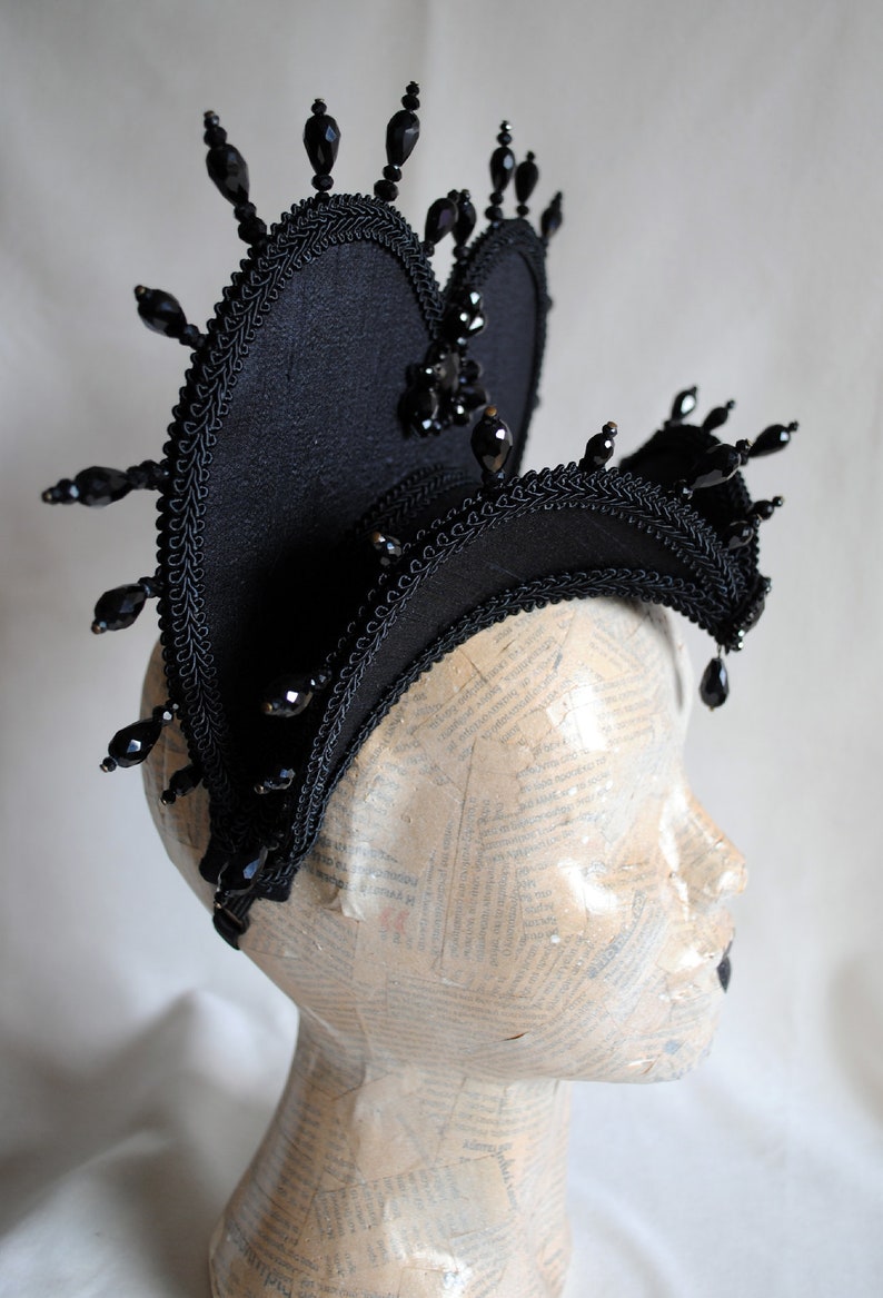 May include: A black fabric headpiece with a heart shape and black bead embellishments.