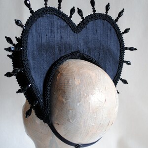 May include: A black fabric heart-shaped headpiece with black bead embellishments. The headpiece has a black elastic band for securing it to the head.