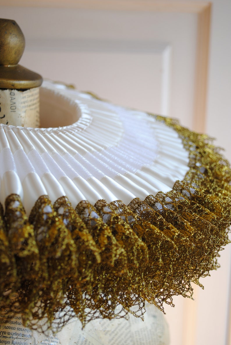 K&ouml;nnte beinhalten: Ein wei&szlig;er R&uuml;schenkragen mit goldener Spitzenborte. Der Kragen ist gefaltet und hat einen zarten, femininen Look.