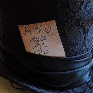 May include: A black top hat with a black satin band and a brown paper tag that says "In this style 10/6".