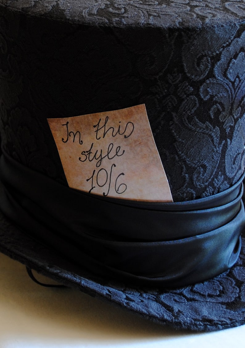 May include: A black top hat with a black satin band and a brown paper tag that says "In this style 10/6".
