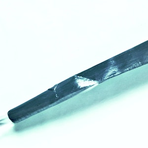 May include: A long, thin, dark grey crystal with a pointed tip. The crystal has a smooth, polished surface and appears to be translucent.