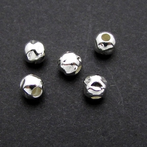 May include: Five silver-toned metal beads with a textured surface and a hole in the center. The beads are arranged in a semi-circle on a dark gray surface.