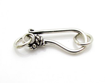 May include: Silver-toned metal clasp with a decorative twist detail. The clasp has a loop on one end and a hook on the other.