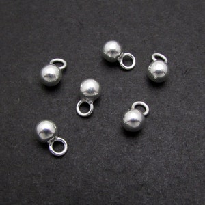 May include: Six silver ball charm pendants with a loop for attaching to jewelry or other crafts.
