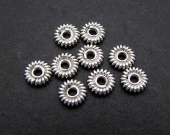 May include: Ten silver-toned metal spacer beads with a decorative, scalloped edge. The beads have a circular shape with a hole in the center.