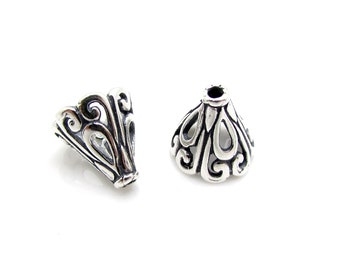 May include: Two silver filigree cone shaped bead caps. The caps have a decorative design with openwork details.