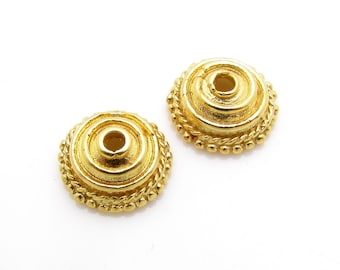 May include: Two gold-toned metal bead caps with a decorative, raised, circular design. The caps have a small hole in the center.