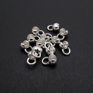 May include: A group of silver-toned metal bead caps with a small loop on each. The bead caps are designed to be used for jewelry making.