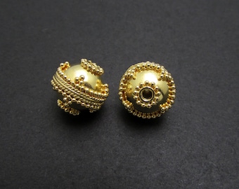 May include: Two gold-colored metal beads with intricate designs. The beads have a round shape and a small hole in the center.