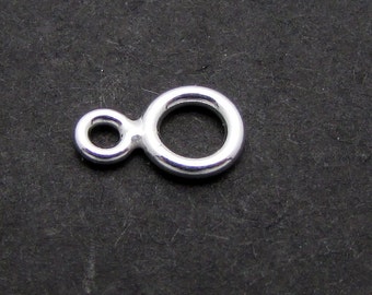 Puede incluir: Un dije conector infinito plateado, con dos bucles circulares conectados. El dije está sobre un fondo oscuro y texturizado. Este componente de joyería es adecuado para crear collares, pulseras y pendientes.