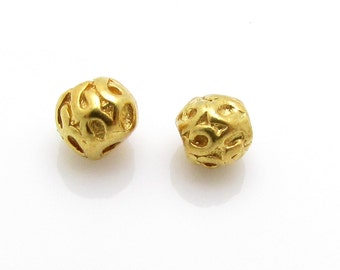 May include: Two gold-colored beads with intricate, raised patterns. The beads are round and have a smooth, polished finish.